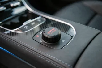 Gros plan sur le bouton AMG Dynamics dans le cockpit d'une Mercedes-AMG, console centrale en cuir noir avec bouton rotatif rouge et argent